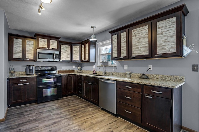 kitchen with appliances with stainless steel finishes, pendant lighting, sink, hardwood / wood-style flooring, and light stone countertops