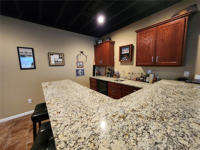 kitchen with kitchen peninsula, light stone counters, sink, dark tile patterned flooring, and a breakfast bar area