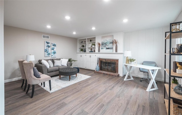 living room with built in shelves, wood-type flooring, and a fireplace