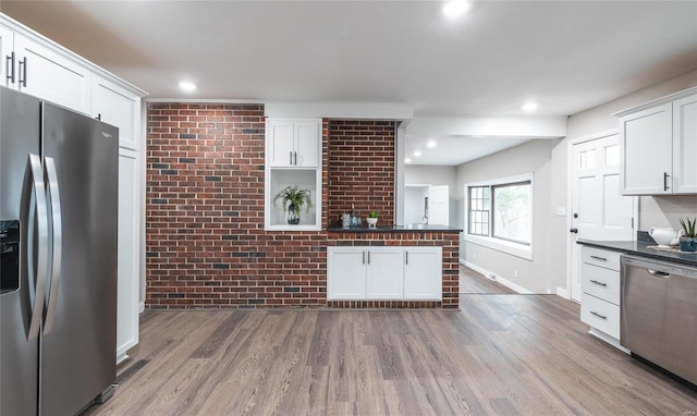 kitchen featuring wood-type flooring, appliances with stainless steel finishes, white cabinetry, and brick wall