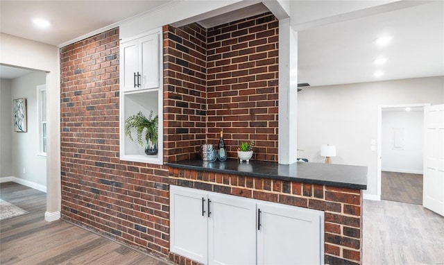 bar featuring white cabinets, hardwood / wood-style floors, and brick wall