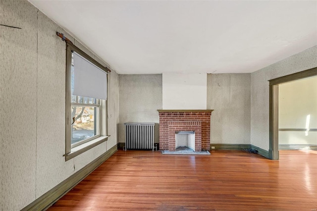 unfurnished living room with wood-type flooring, radiator, and a brick fireplace