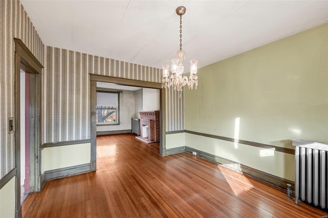 unfurnished dining area with hardwood / wood-style floors, radiator heating unit, a chandelier, and a brick fireplace