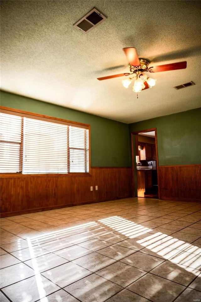 empty room featuring tile patterned floors, wood walls, and ceiling fan