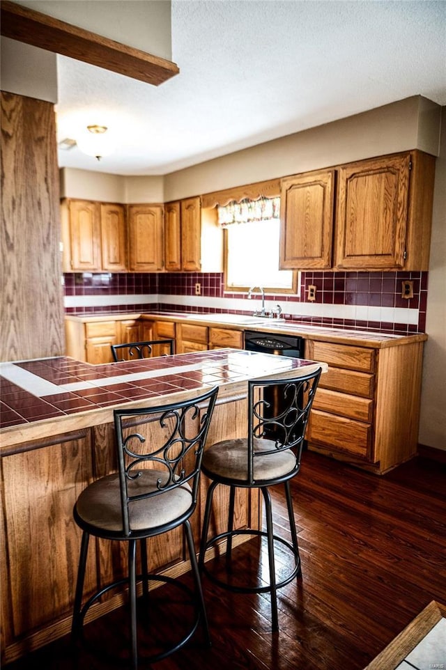 kitchen featuring a breakfast bar, tasteful backsplash, dishwasher, and dark wood-type flooring