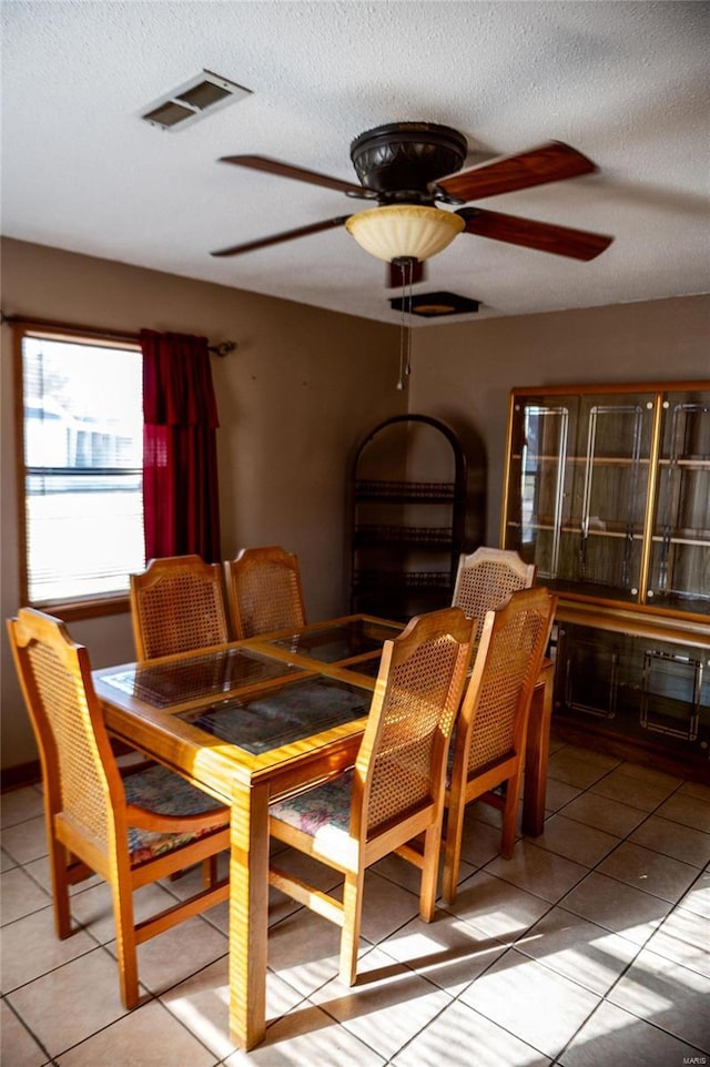 dining area featuring ceiling fan, light tile patterned flooring, and a textured ceiling