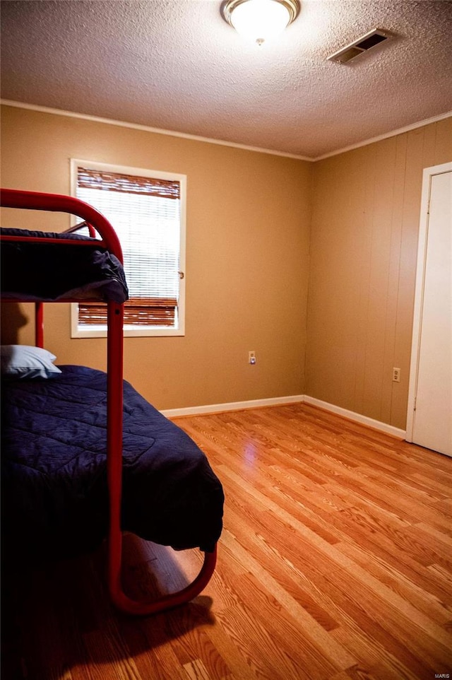 bedroom featuring a textured ceiling, light hardwood / wood-style flooring, and crown molding