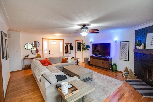 living room with a textured ceiling, ceiling fan, a fireplace, and light hardwood / wood-style flooring