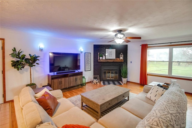 living room with a textured ceiling, light hardwood / wood-style floors, a brick fireplace, and ceiling fan