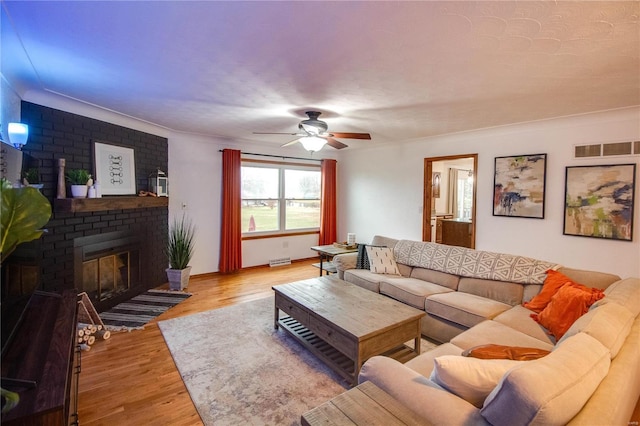 living room with ceiling fan, a fireplace, crown molding, and light wood-type flooring