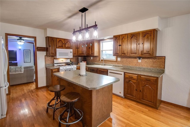 kitchen with light wood-type flooring, white appliances, sink, a center island, and hanging light fixtures