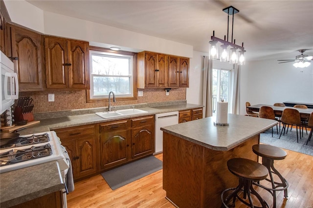 kitchen with sink, pendant lighting, white appliances, a kitchen island, and light wood-type flooring