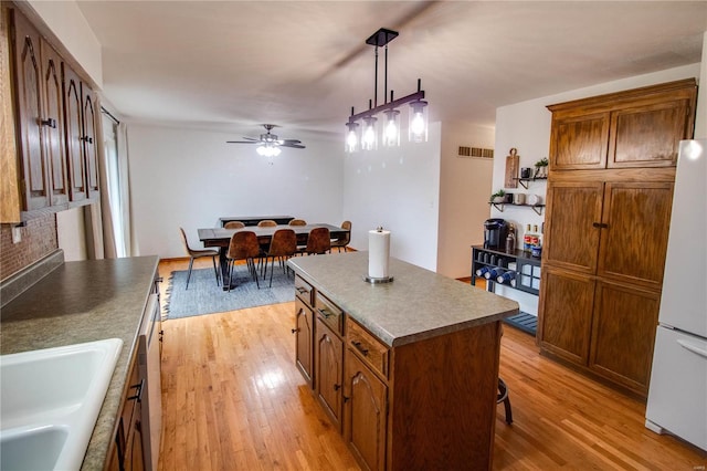 kitchen featuring pendant lighting, a center island, sink, light hardwood / wood-style flooring, and white fridge