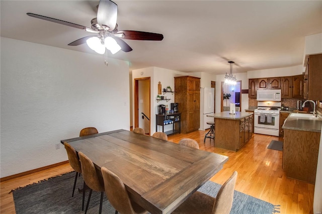 dining area featuring sink, ceiling fan with notable chandelier, and light wood-type flooring