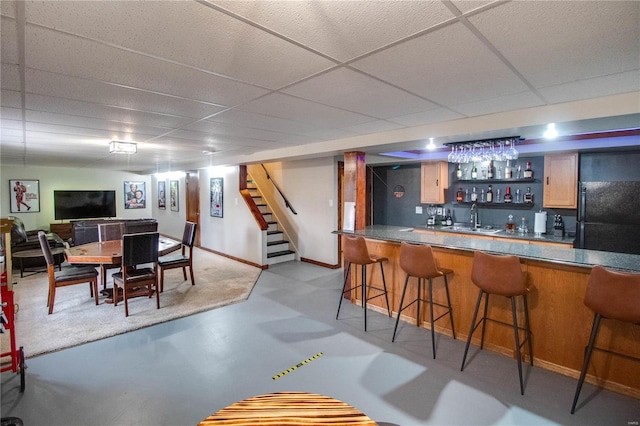 bar featuring a paneled ceiling, black fridge, and sink