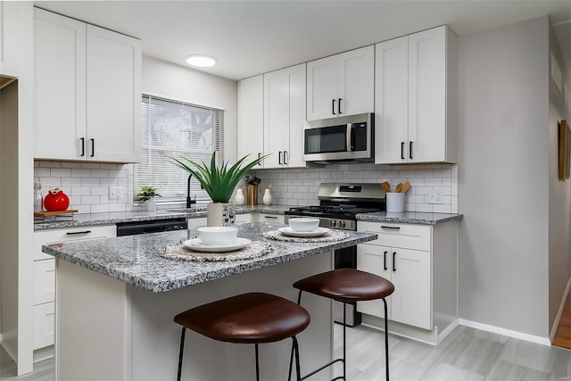 kitchen with decorative backsplash, white cabinetry, light stone counters, and appliances with stainless steel finishes