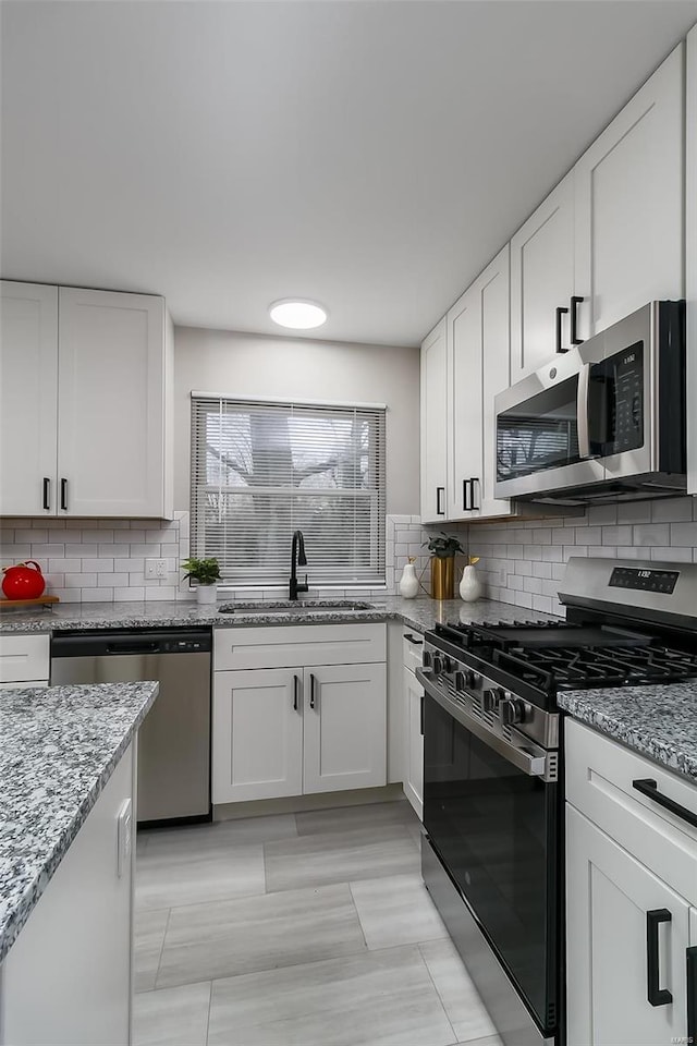 kitchen with tasteful backsplash, sink, white cabinets, and appliances with stainless steel finishes