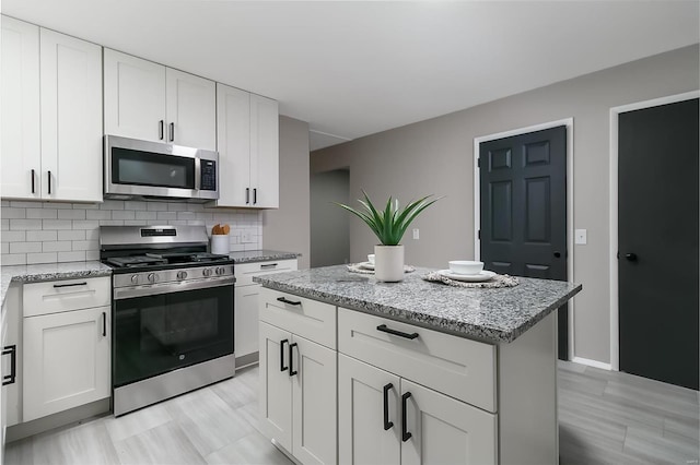 kitchen featuring decorative backsplash, light stone counters, stainless steel appliances, a kitchen island, and white cabinetry