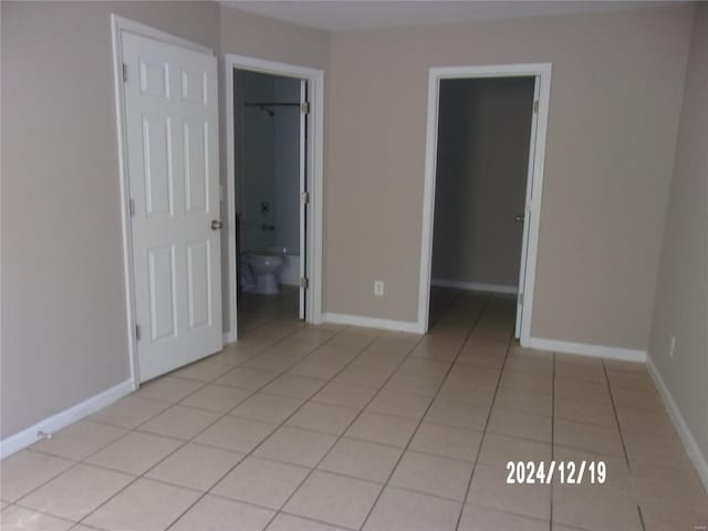 unfurnished bedroom featuring light tile patterned floors, a walk in closet, a closet, and connected bathroom