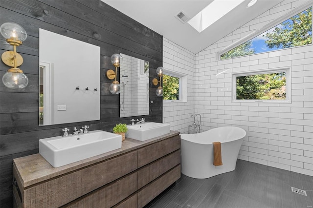 bathroom featuring vaulted ceiling with skylight, a freestanding tub, double vanity, and a sink