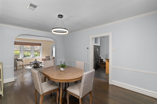 dining room featuring arched walkways, visible vents, crown molding, and dark wood-style flooring