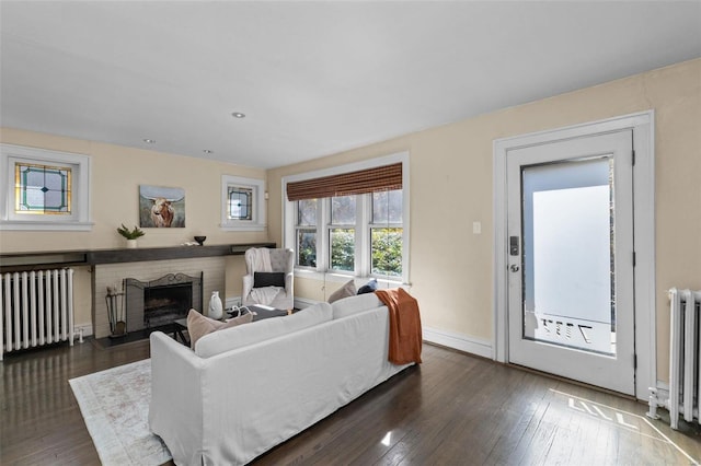 living room with baseboards, radiator, a brick fireplace, and dark wood-style flooring