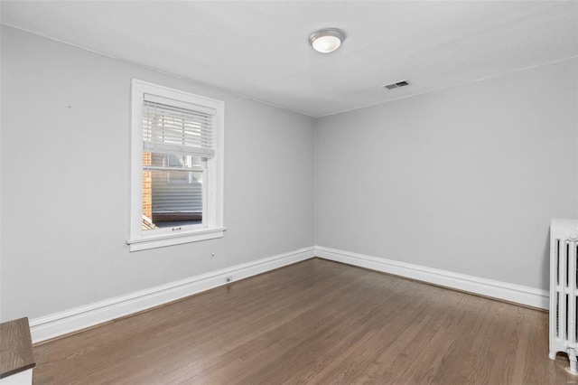 spare room with visible vents, radiator heating unit, baseboards, and wood finished floors