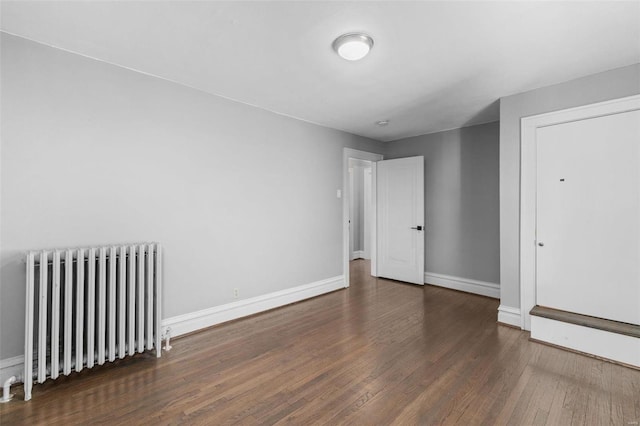 unfurnished bedroom with radiator heating unit, wood finished floors, and baseboards