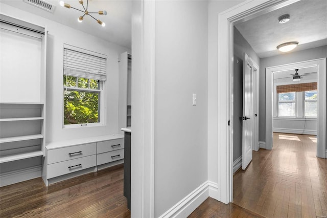 corridor featuring a notable chandelier, dark wood-style floors, visible vents, and baseboards