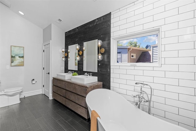 bathroom featuring a freestanding bath, double vanity, toilet, and a sink