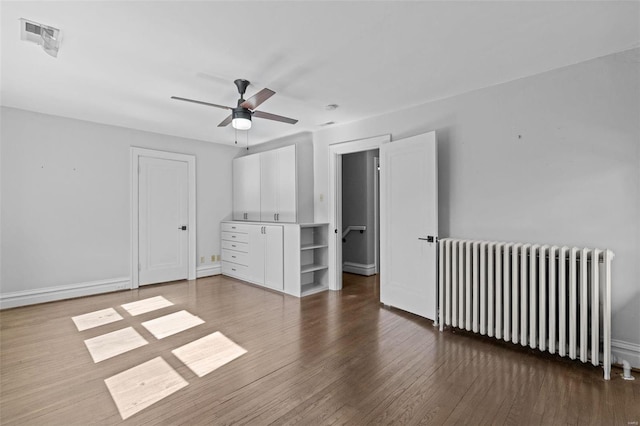 unfurnished bedroom featuring radiator, wood finished floors, visible vents, baseboards, and ceiling fan