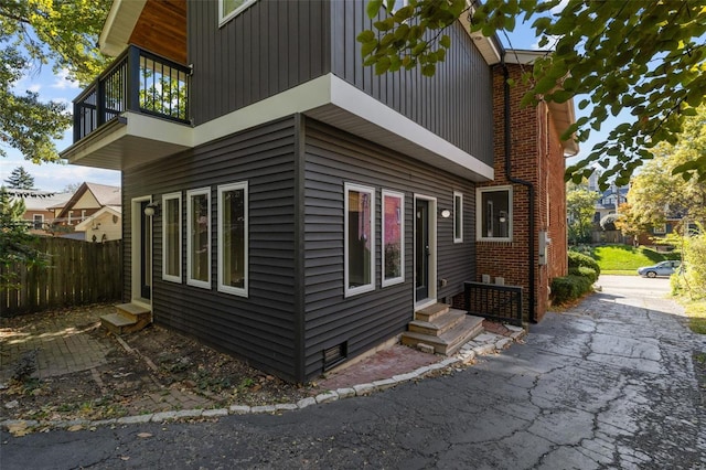 view of property exterior with entry steps, a balcony, and fence