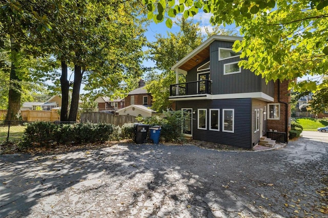 exterior space with brick siding, a balcony, entry steps, and fence