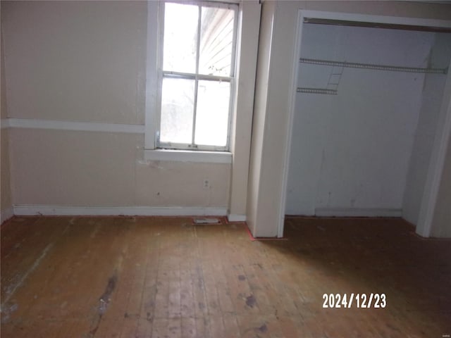 unfurnished bedroom featuring wood-type flooring, multiple windows, and a closet