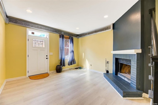 foyer entrance featuring light wood-type flooring, a brick fireplace, and ornamental molding