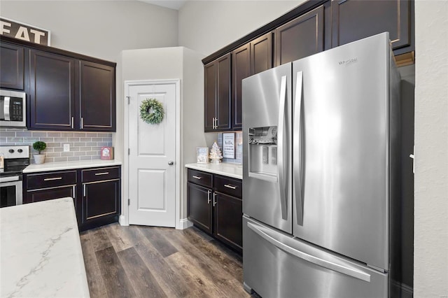 kitchen with tasteful backsplash, dark brown cabinets, dark hardwood / wood-style flooring, stainless steel appliances, and light stone countertops