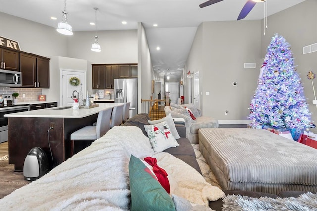 kitchen featuring decorative light fixtures, a center island with sink, appliances with stainless steel finishes, a towering ceiling, and backsplash