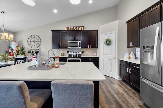 kitchen with stainless steel appliances, an island with sink, lofted ceiling, and decorative light fixtures