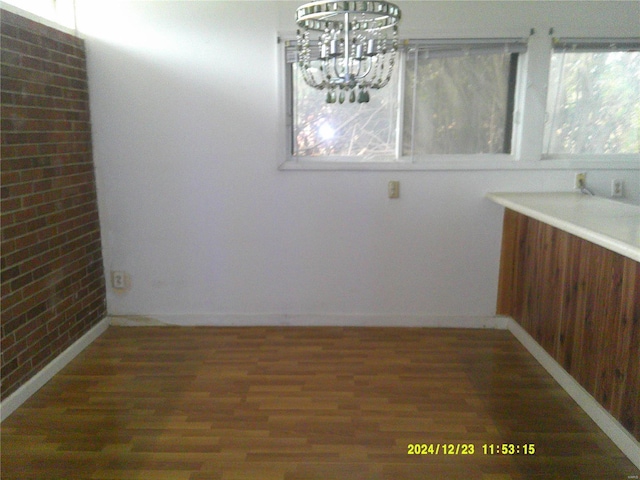 unfurnished dining area featuring a notable chandelier, dark hardwood / wood-style flooring, and brick wall