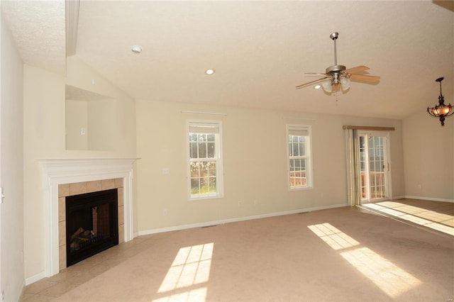 unfurnished living room featuring a tile fireplace, light carpet, ceiling fan with notable chandelier, and vaulted ceiling