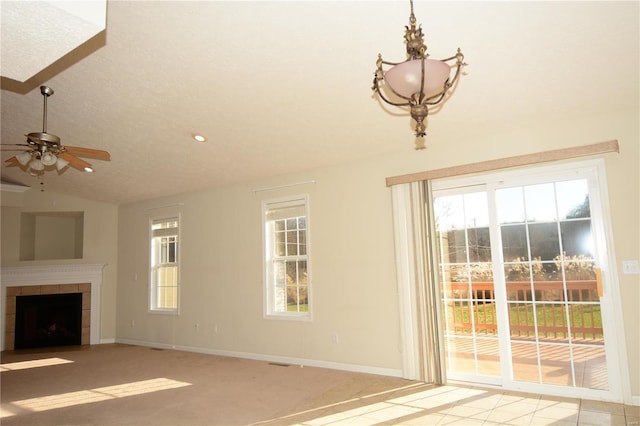 unfurnished living room with ceiling fan, a tile fireplace, and vaulted ceiling