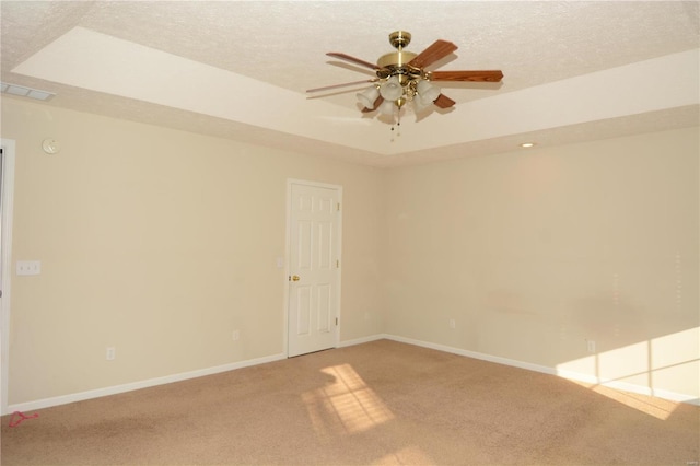 unfurnished room featuring a raised ceiling, ceiling fan, carpet floors, and a textured ceiling