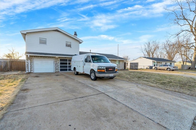 view of front of house featuring driveway, stone siding, a chimney, an attached garage, and fence