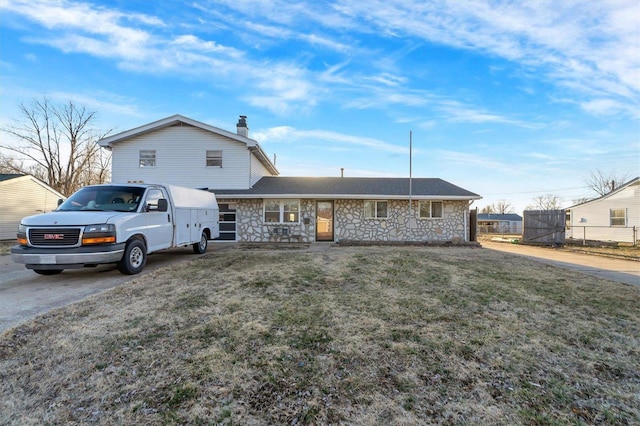 view of front of home with a chimney, fence, stone siding, driveway, and a front lawn