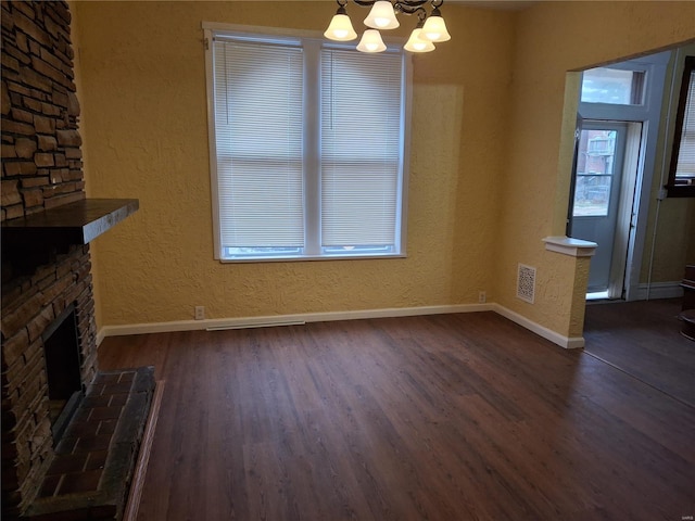 unfurnished living room with dark hardwood / wood-style flooring, a wealth of natural light, a fireplace, and a notable chandelier