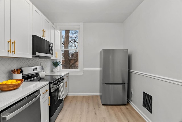 kitchen with stainless steel appliances, light stone counters, backsplash, light hardwood / wood-style floors, and white cabinets