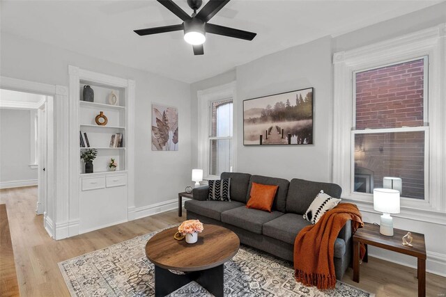 living room with built in shelves, ceiling fan, and light wood-type flooring