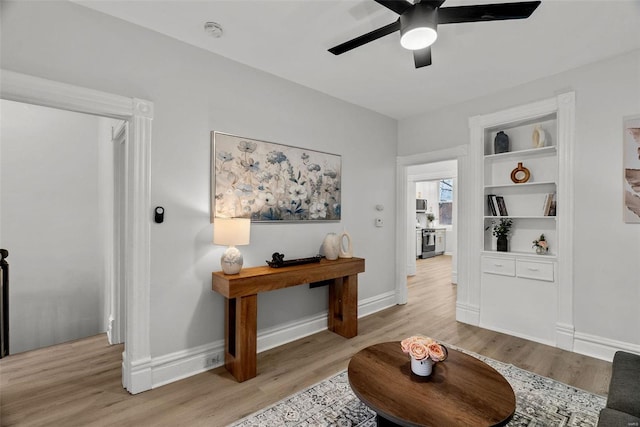 sitting room featuring built in shelves, ceiling fan, and light hardwood / wood-style flooring