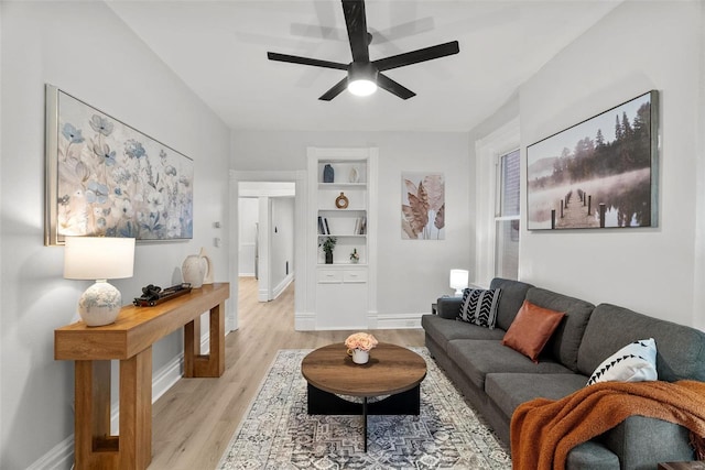 living room featuring built in shelves, ceiling fan, and light wood-type flooring