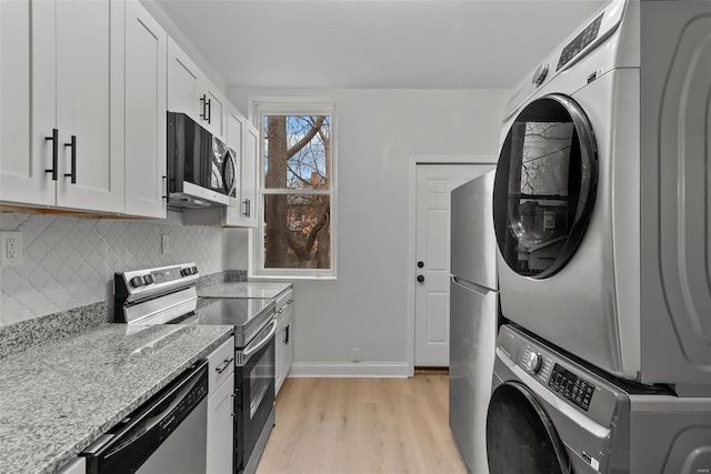 kitchen featuring white cabinetry, stacked washer and dryer, light stone countertops, and appliances with stainless steel finishes